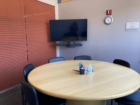 Room with large round table, 8 chairs, and an LCD screen.