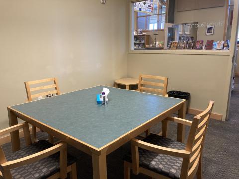 A square table with four chairs; a small table is in the background.