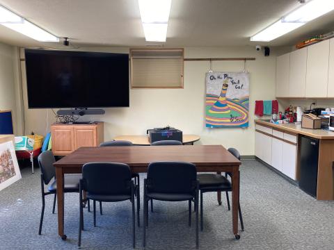 A room with 1 table and 4 chairs, LCD screen, and kitchen sink area