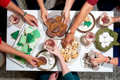 Plates filled with cookies and hands reaching to take them.