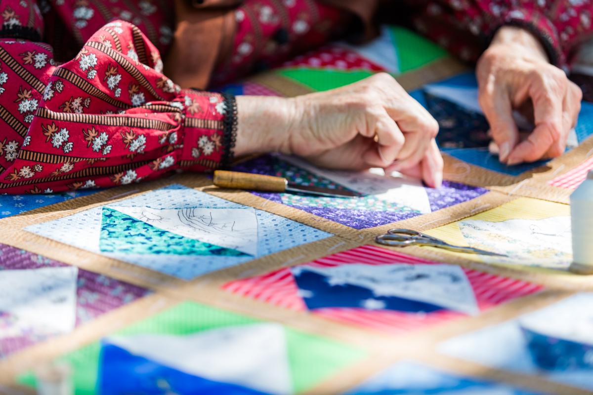 Colorful quilt on table with a pair of adult hands putting a square in place