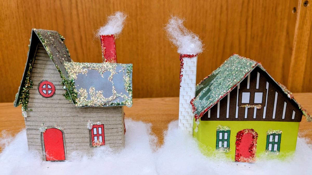 Two tiny Putz cardboard houses decorated in wintery faux snow and glitter.